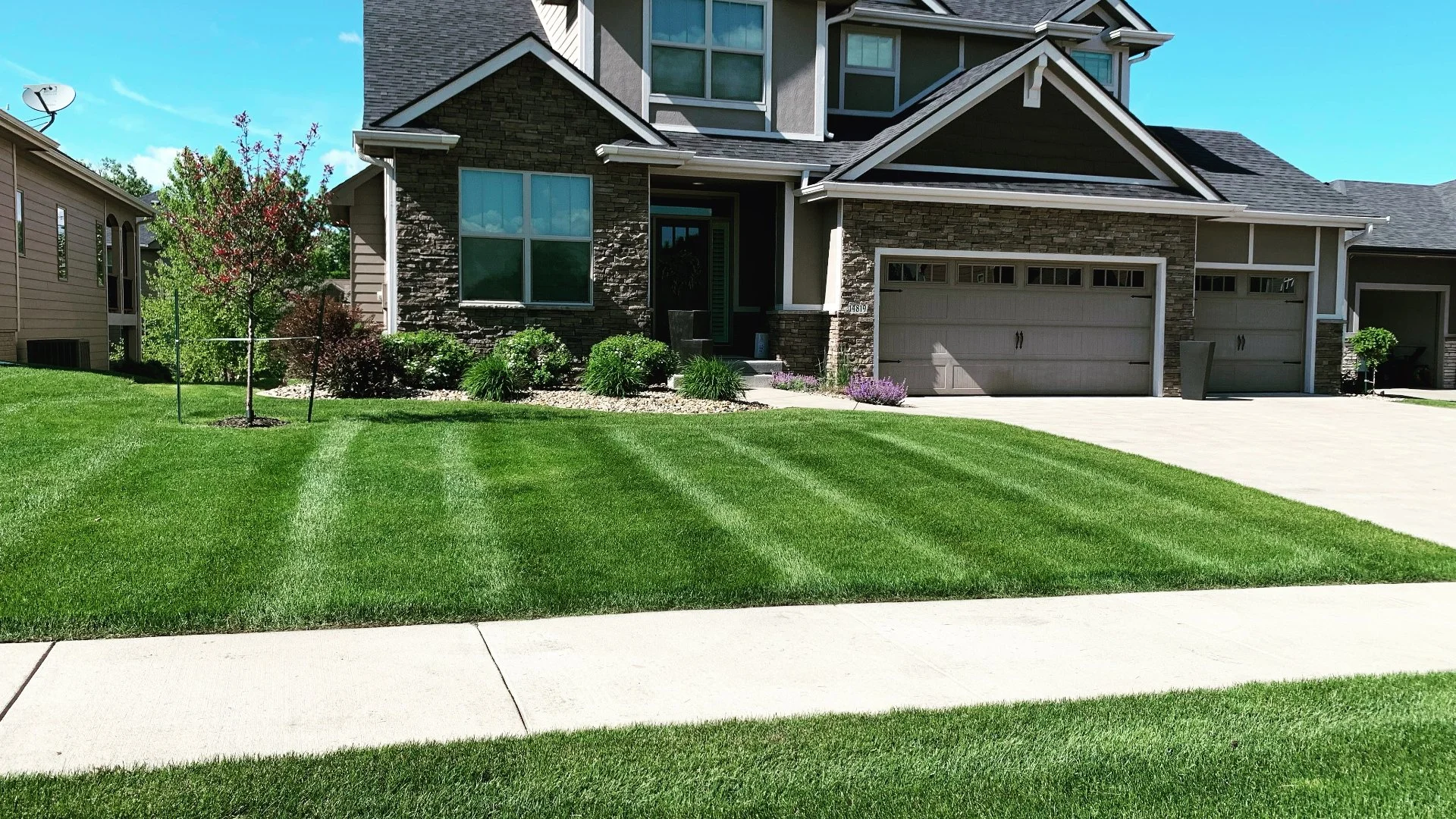 A well-maintained, vibrant green lawn with striped mowing patterns and clean landscaping.