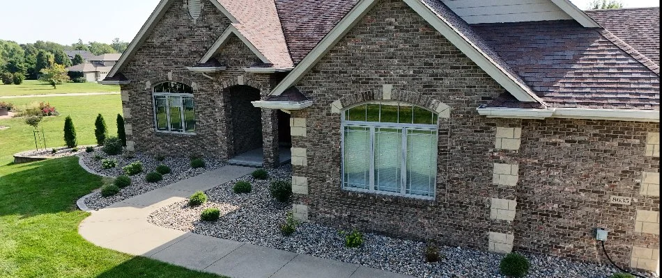 Aerial view of a brick home with a landscaped entrance, featuring a curved walkway, decorative stone, and flower beds surrounding the front yard