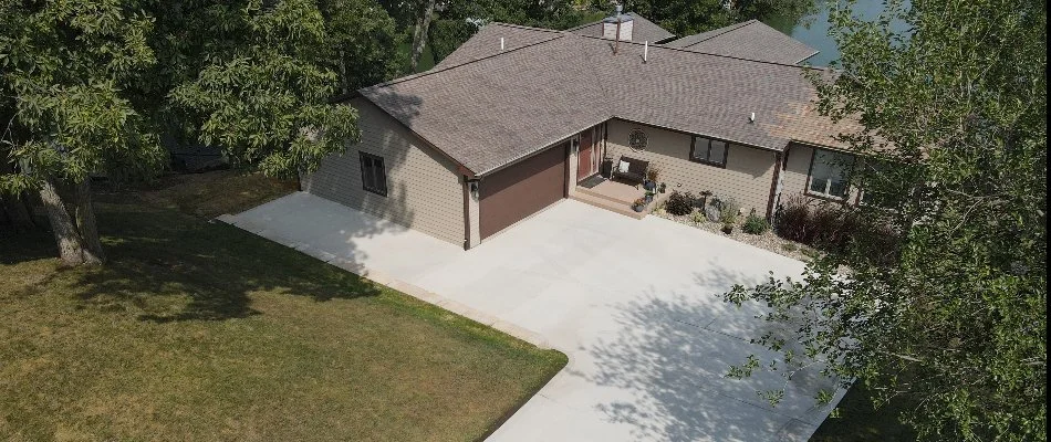 Aerial view of a modern home with a concrete driveway, surrounded by greenery, showcasing an open lawn and a clear view of the house