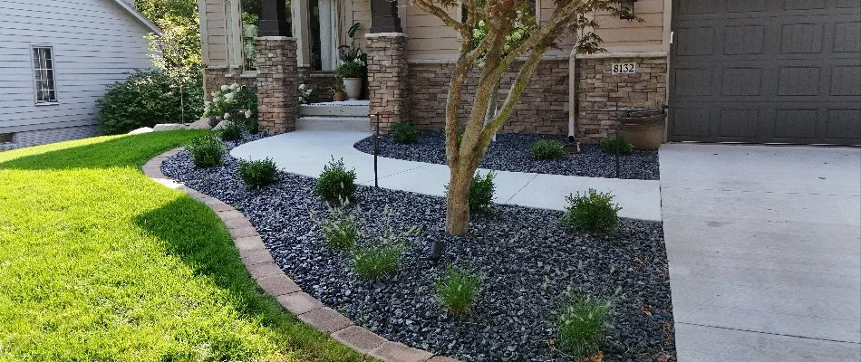 Close-up view of a landscaped front yard with a walkway leading to a modern home's entrance, featuring stone accents, decorative plants, and grassy areas