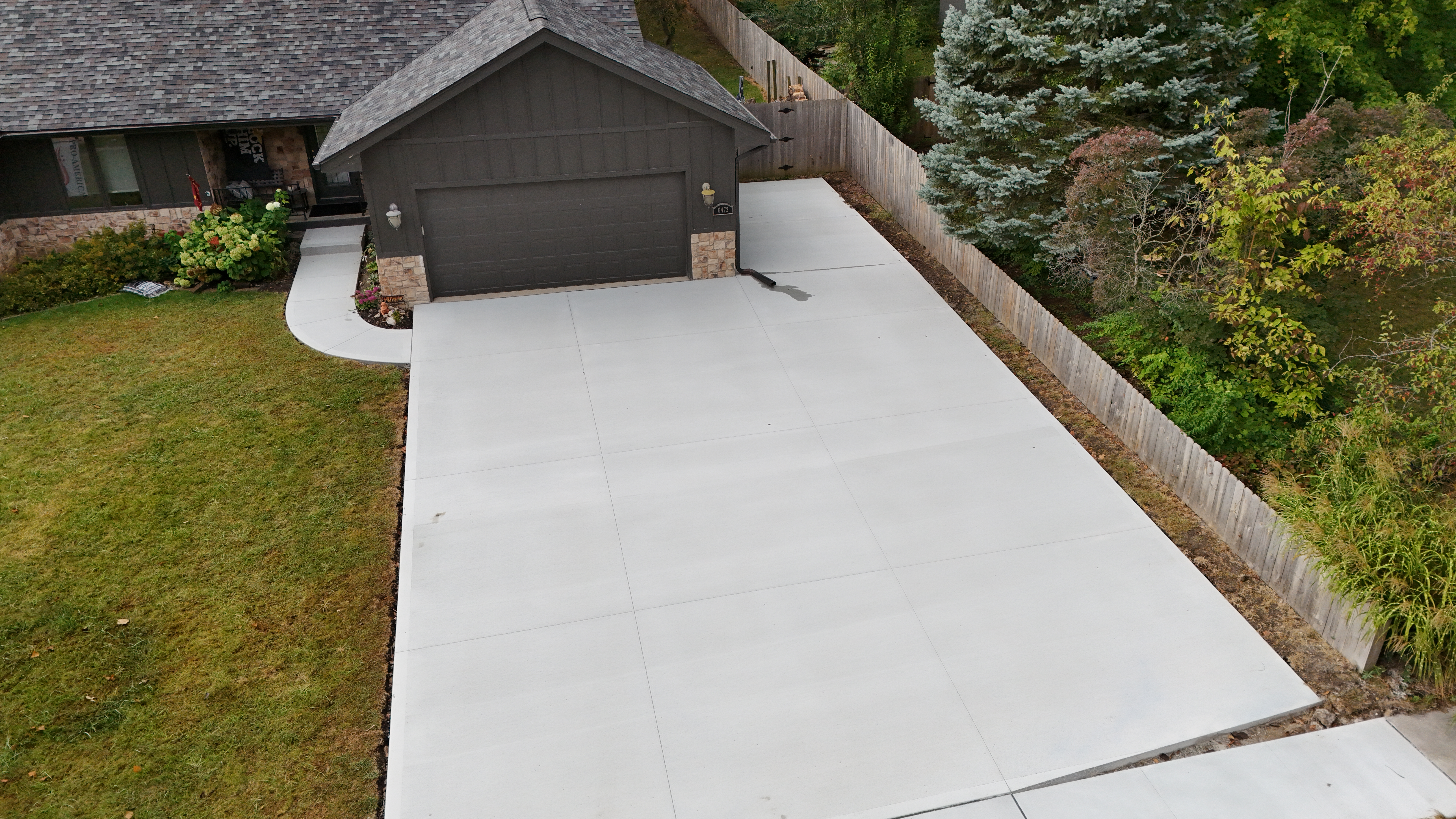 Aerial view of a residential driveway with new concrete, surrounded by green grass and landscaped garden